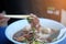 Man hand uses chopsticks to pickup pork in thai noodles bowl on the table