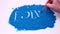 Man hand writing phrase follow us on a blue art sand. Studio footage on a white background.