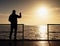 Man at handrail on mole take photos over sea to morning horizon. Tourist photograph