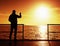 Man at handrail on mole take photos over sea to morning horizon. Tourist photograph