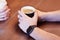 The man hands with black electronic watch, holding black cup of coffee. Other hands on background with white cup, wooden table. Da