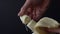 Man hands breaks off a piece of ripe banana on a dark background close-up