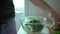 Man hands putting chopped green herbs in glass bowl