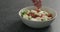 Man hands salting salad with mozzarella, cherry tomatoes and frisee leaves in white bowl on terrazzo surface