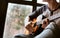 Man hands sitting on the big window windowsil and playing on guitar - fingers close up image