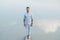 Man handsome stands on wooden bridge and looks at the water reflex of blue sky. Concept of freedom relaxation. Place for text or