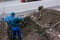 A man handyman digs a trench in the winter in the city by hand with a shovel.