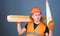 Man, handyman in helmet, hard hat holds handsaw, looks at sharp blade, grey background. Carpenter concept. Carpenter