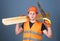 Man, handyman in helmet, hard hat holds handsaw and wooden beams, grey background. Woodcraft concept. Carpenter