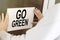 A man hangs a notice on a glass door with the text Go Green