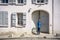 Man in hat peers into the courtyard of the house with shutters through slightly open gate