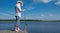 A man in a hat, on the pier, holding spinning, for fishing, against a blue lake and sky