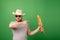 A man in a hat and sunglasses shows a French baguette on a green background