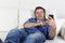 Man having fun alone lying on home couch listening to music with mobile phone and headphones