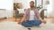 Man in headphones meditating in lotus pose at home