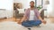 Man in headphones meditating in lotus pose at home