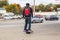 Man with helmet and backback on one wheel motorized skateboard on sidewalk in urban area with cars on stree and stores and fall