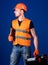 Man in helmet, hard hat holds toolbox and folder with documents, blue background. Repairman ready to work. Repair