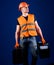 Man in helmet, hard hat holds toolbox and suitcase with tools, blue background. Handyman, repairman on dreamy face goes