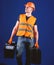 Man in helmet, hard hat holds toolbox and suitcase with tools, blue background. Handyman, repairman on dreamy face goes