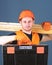 Man in helmet, hard hat holds toolbox and wooden beams, grey background. Professional woodworker concept. Carpenter