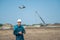 A man in a helmet and overalls controls a drone at a construction site. The builder carries out technical oversight.