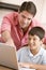 Man helping young boy in kitchen with laptop