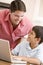 Man helping young boy in kitchen with laptop