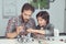 A man helps a boy with a robot assembly. The boy looks carefully as a man collects a robot