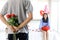 Man hiding beautiful red rose bouquet behind back, ready to give Valentine flower present to lover girlfriend for celebration,