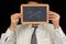 Man hiding his face with a school slate on which is drawn a sad face