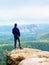 Man hiker in dark sportswear and poles stand on mountain peak rock. Exposed sandstone cliff