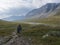 Man hiker with heavy backpack in wild Lapland nature with blue glacial river, birch tree bushes, snow capped mountains and