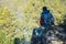 Man hiker with a large backpack sitting on a rock cliff and looking at the sprawling green valley. Freedom in travel