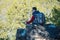 Man hiker with a large backpack sitting on a rock cliff and looking at the sprawling green valley. Freedom in travel