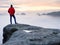 Man hiker at mountain peak. Marvelous daybreak in autumn misty landscape. Sun hidden in clouds