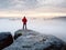 Man hiker at mountain peak. Marvelous daybreak in autumn misty landscape. Sun hidden in clouds