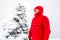 A man/hiker with red jacket and norwegian flag on his chest standing on a snowy mountain peak next to a frozen cairn.