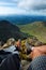 Man hiker sitting on the top of mountain rocks. Beautiful weather with Scotland nature. Detail of hiking boots on the difficult pa