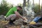 Man in hiking clothes heats a metal prefabricated burner with wood, for cooking, in the forest, in a camp. Active rest.