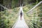 Man hiking with dog crossing long suspension bridge in the woods of Canadian Rockies, narrow shot