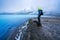 Man with hiking gear stands on shore looking towards Geothermal powerplant at the blue lagoon in Jarabodin/Myvatn