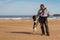 A man and his dog look at each other on the beach.