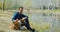 Man with his dog outdoors, sit beside river in park alone. Pensive calm look.