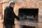 Man in his forties is preparing the charcoal with burned firewood in the barbecue before cooking.