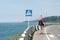 Man with his son on their shoulders walks along the highway against the background of the sea. Pedestrian crossing sign