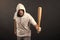 Man hold baseball bat, agression. Hooligan wear hood in hoody, fashion. Gangster guy threaten with bat weapon