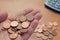 A man hold a buch of two euro cent coins in the palm of his hand over a table with other coins and a calculator