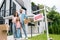 Man holding box and standing with wife and daughter near house and board with sold letters