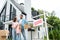 Man holding box and standing with wife and daughter near house and board with sold letters